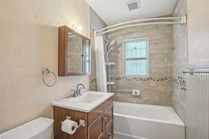 Bathroom with bathing tub / shower combination, visible vents, a textured wall, toilet, and vanity