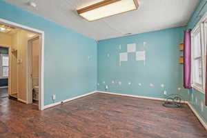 Unfurnished room featuring baseboards, visible vents, dark wood finished floors, and a textured ceiling