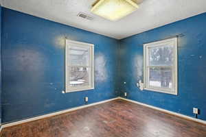 Empty room featuring a textured ceiling, wood finished floors, visible vents, and baseboards