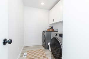 Clothes washing area featuring cabinet space, baseboards, visible vents, washer and clothes dryer, and light wood-type flooring