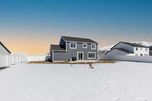 Snow covered back of property with a fenced backyard