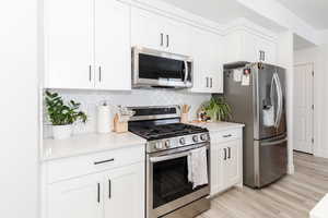 Kitchen featuring backsplash, white cabinetry, stainless steel appliances, and light countertops