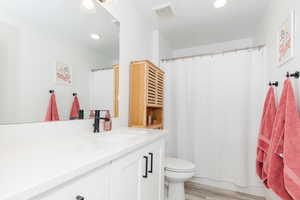 Bathroom featuring visible vents, toilet, wood finished floors, vanity, and recessed lighting