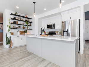 Kitchen featuring stainless steel appliances, white cabinetry, light countertops, a center island with sink, and pendant lighting