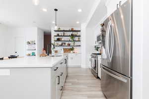 Kitchen with stainless steel appliances, white cabinetry, light countertops, a center island with sink, and pendant lighting