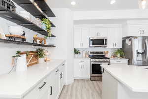 Kitchen with stainless steel appliances, open shelves, light countertops, and white cabinets