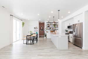 Kitchen featuring decorative light fixtures, a center island with sink, light countertops, appliances with stainless steel finishes, and a sink