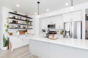 Kitchen featuring appliances with stainless steel finishes, light countertops, a sink, and hanging light fixtures