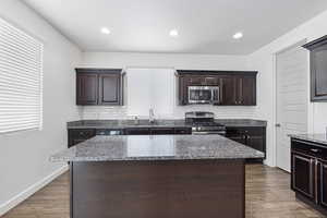 Kitchen with stainless steel appliances, light stone counters, a sink, and a center island