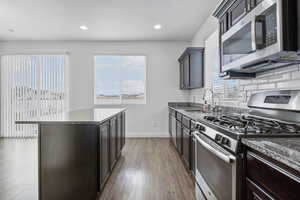 Kitchen with a kitchen island, a sink, appliances with stainless steel finishes, light wood-type flooring, and backsplash