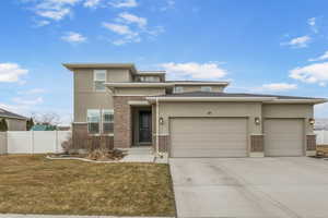 Prairie-style home with brick siding, fence, an attached garage, and stucco siding