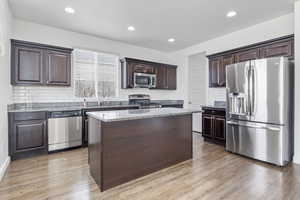 Kitchen with dark brown cabinetry, light wood-style flooring, a kitchen island, stainless steel appliances, and a sink