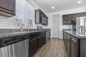 Kitchen with appliances with stainless steel finishes, dark stone countertops, dark brown cabinetry, and light wood-style floors