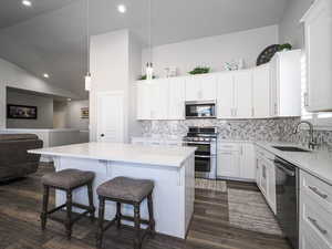 Kitchen featuring light countertops, appliances with stainless steel finishes, decorative light fixtures, and white cabinets