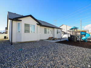 Rear view of property featuring a playground, central air condition unit, fence, roof with shingles, and stucco siding