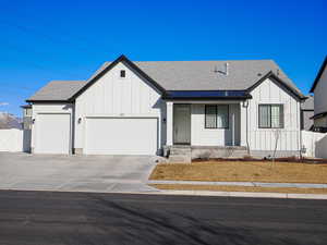 Modern farmhouse featuring concrete driveway, roof with shingles, an attached garage, fence, and board and batten siding