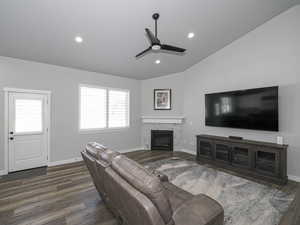 Living area with dark wood-style floors, a tile fireplace, vaulted ceiling, and baseboards