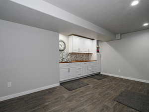 Kitchen with dark wood-style floors, recessed lighting, decorative backsplash, white cabinets, and baseboards