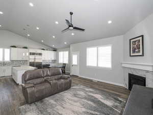 Living room with dark wood-style floors, a tiled fireplace, vaulted ceiling, ceiling fan, and baseboards