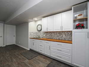 Kitchen with white cabinets, dark wood-style flooring, a sink, wooden counters, and backsplash