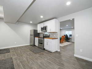 Kitchen featuring decorative backsplash, wood counters, dark wood-style flooring, stainless steel appliances, and white cabinetry