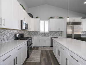 Kitchen with lofted ceiling, appliances with stainless steel finishes, decorative light fixtures, light countertops, and white cabinetry