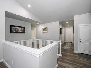 Hallway featuring recessed lighting, vaulted ceiling, dark wood-type flooring, and an upstairs landing