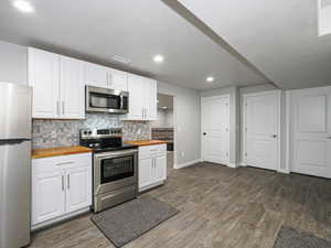 Kitchen with decorative backsplash, butcher block countertops, appliances with stainless steel finishes, dark wood-type flooring, and white cabinetry