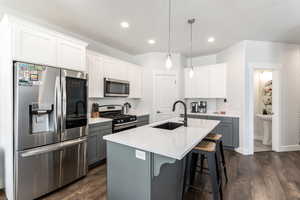 Kitchen featuring gray cabinetry, a sink, white cabinets, appliances with stainless steel finishes, and a center island with sink