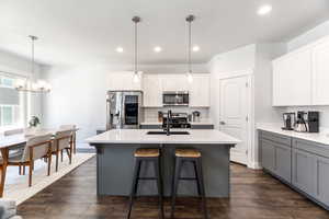 Kitchen with a kitchen island with sink, stainless steel appliances, light countertops, white cabinetry, and pendant lighting