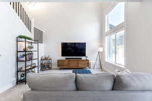 Living area with carpet, baseboards, visible vents, and a high ceiling