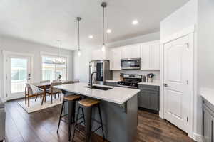 Kitchen with stainless steel appliances, light countertops, hanging light fixtures, gray cabinetry, and a sink