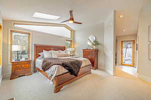 Bedroom featuring vaulted ceiling with skylight, light colored carpet, baseboards, and multiple windows