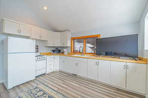 Kitchen featuring lofted ceiling, white appliances, a sink, white cabinets, and light countertops