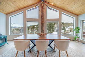 Dining room featuring light wood-type flooring, a wood stove, wooden ceiling, and vaulted ceiling