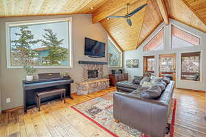 Living room featuring wood ceiling, a stone fireplace, beamed ceiling, and light wood-style flooring