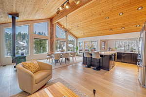 Living area with high vaulted ceiling, wood ceiling, light wood-style floors, beamed ceiling, and a wood stove