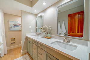 Full bathroom featuring double vanity, heating unit, a sink, and wood finished floors