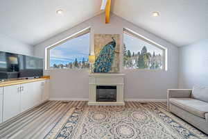 Living area featuring a fireplace with raised hearth, light wood finished floors, a textured ceiling, and baseboards