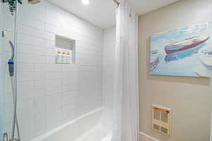 Bathroom with shower / bath combination with curtain, a textured wall, and heating unit