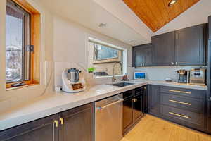 Kitchen with lofted ceiling, wooden ceiling, light wood-style flooring, a sink, and stainless steel dishwasher