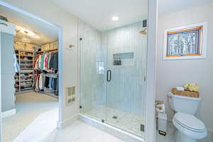 Bathroom with heating unit, a spacious closet, toilet, a stall shower, and baseboards