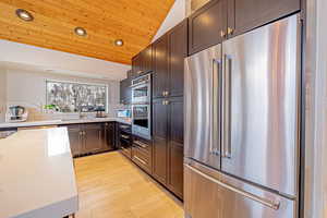 Kitchen with wooden ceiling, appliances with stainless steel finishes, light stone countertops, vaulted ceiling, and a sink