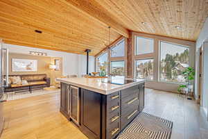 Kitchen with light stone counters, wine cooler, hanging light fixtures, wood ceiling, and light wood-type flooring