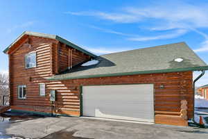 View of property exterior with aphalt driveway, roof with shingles, an attached garage, and log siding