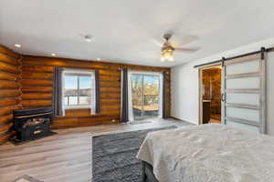 Unfurnished bedroom with a barn door, access to outside, light wood finished floors, rustic walls, and a wood stove