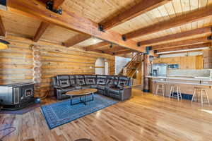 Living room featuring log walls, wood ceiling, a wood stove, light wood-type flooring, and stairs