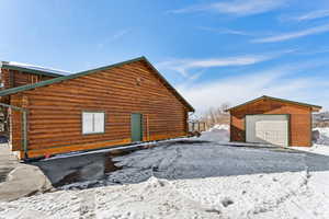 Snow covered property with a garage, log exterior, and an outbuilding