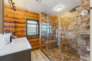 Full bath with a stall shower, rustic walls, vanity, and wood finished floors