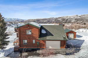 View of snow covered exterior featuring a shingled roof, log siding, and a mountain view